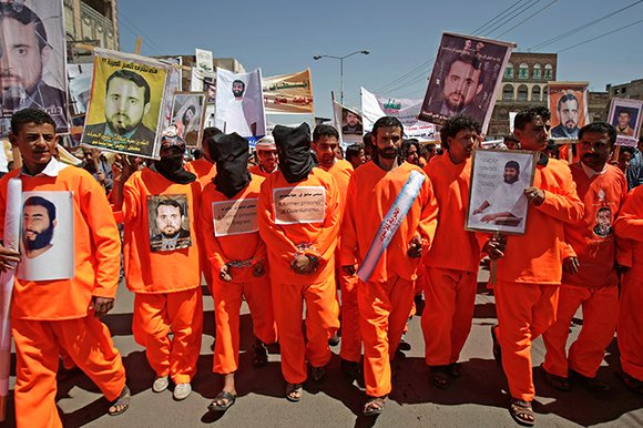 Yemeni protestors dressed in prison uniforms, hold posters of men detained in Guantanamo Bay prison during a demonstration in front of the U.S. embassy demanding their release, in Sanaa, Yemen, Tuesday, April 16, 2013.