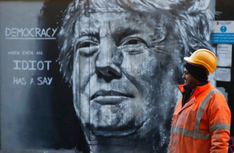 A construction worker stands in front of a piece of street art portraying prospective U.S. Presidential candidate Donald Trump, in east London